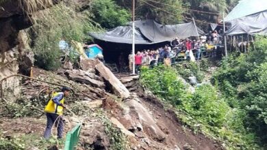 Rescue worker clearing debris after Uttarakhand Cloudburst, with people watching from a safe distance near damaged tents.